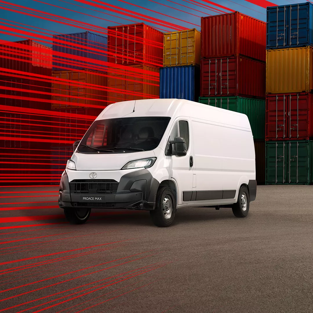 Ein Mann in Arbeitskleidung entfernt sich von einem weißen Proace Max in einer Lagerhalle mit hohen Regalen und vielen Kartons.